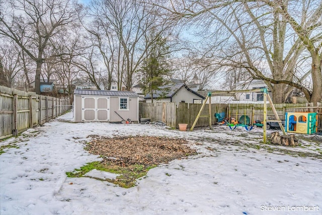 yard covered in snow featuring a fenced backyard, a storage unit, a playground, and an outbuilding