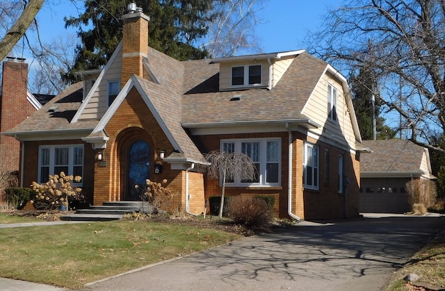 view of front of house featuring an outbuilding, brick siding, roof with shingles, a chimney, and an attached garage