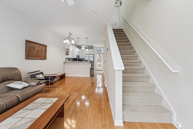 living area featuring stairs, light wood finished floors, and a ceiling fan