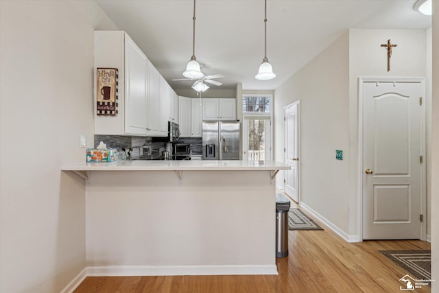 kitchen featuring light countertops, light wood-style flooring, decorative backsplash, appliances with stainless steel finishes, and a peninsula