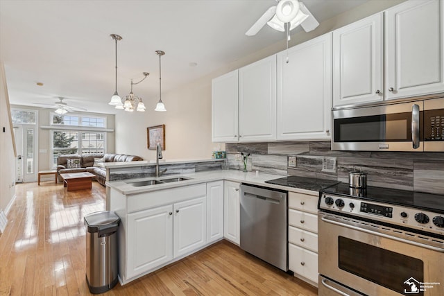 kitchen with stainless steel appliances, a peninsula, a sink, and white cabinets