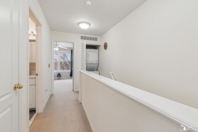 corridor with visible vents, stacked washer / dryer, light carpet, an upstairs landing, and baseboards