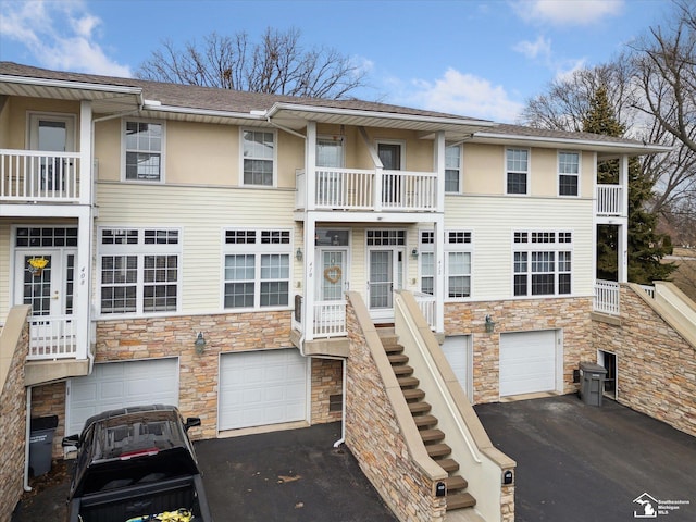 view of property with driveway, a garage, stone siding, stairs, and stucco siding