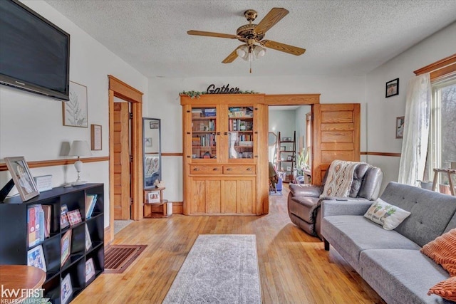 living area with wood-type flooring, ceiling fan, and a textured ceiling