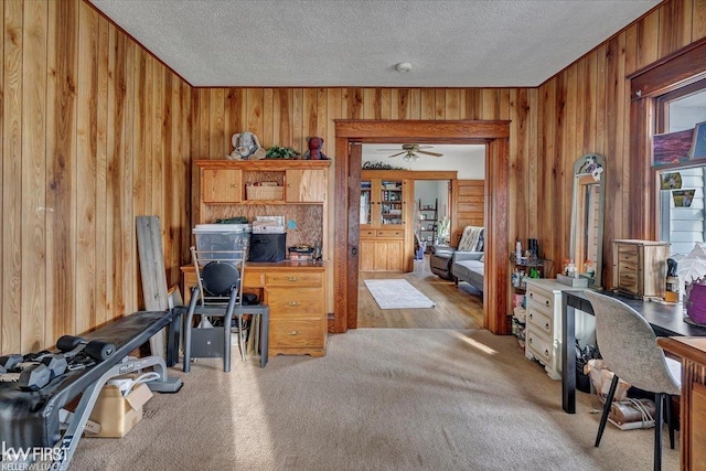 home office with carpet, wooden walls, a ceiling fan, and a textured ceiling