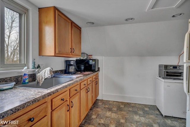 kitchen with brown cabinets, lofted ceiling, stone finish flooring, a sink, and baseboards