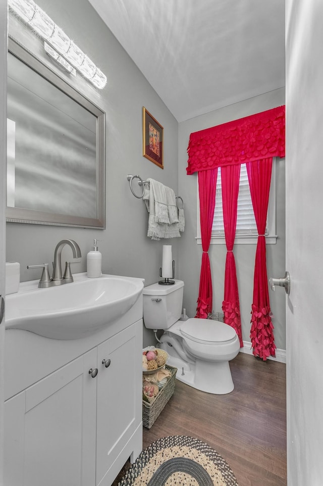 half bath featuring toilet, vanity, baseboards, and wood finished floors