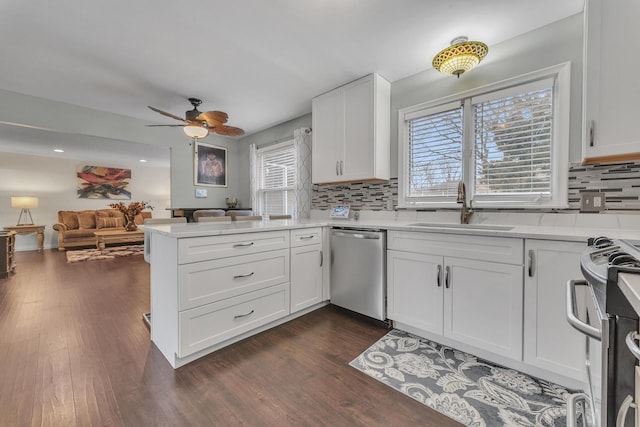 kitchen featuring a sink, open floor plan, appliances with stainless steel finishes, a peninsula, and dark wood-style flooring