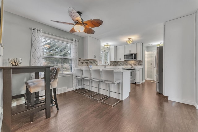 kitchen with a peninsula, dark wood-style flooring, stainless steel appliances, light countertops, and tasteful backsplash