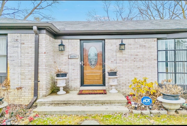 property entrance featuring brick siding and a shingled roof