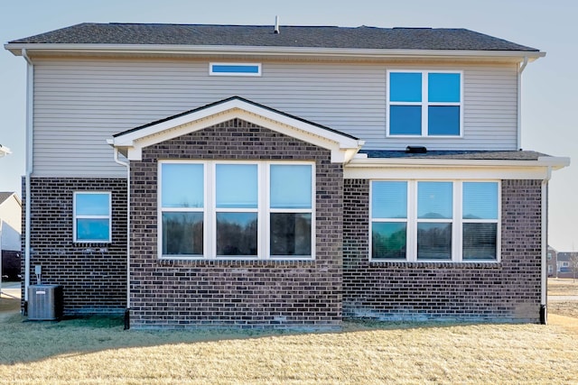 rear view of house featuring brick siding, central AC unit, and a lawn