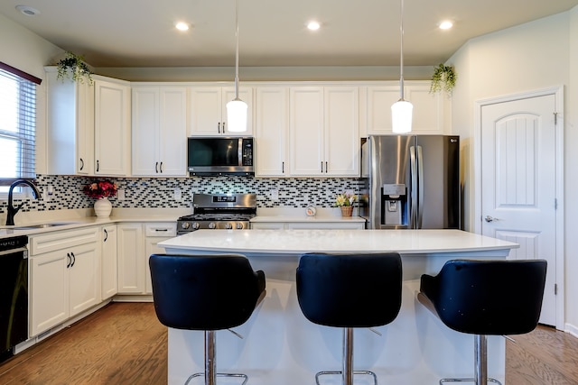 kitchen featuring a breakfast bar area, a sink, light countertops, light wood-style floors, and appliances with stainless steel finishes