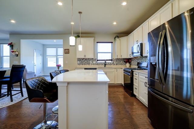 kitchen featuring dark wood-type flooring, a sink, a center island, appliances with stainless steel finishes, and light countertops