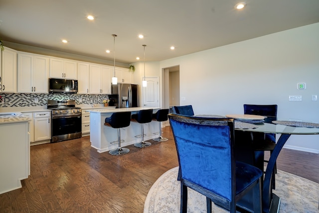 kitchen with a kitchen bar, backsplash, a kitchen island, stainless steel appliances, and dark wood-style flooring