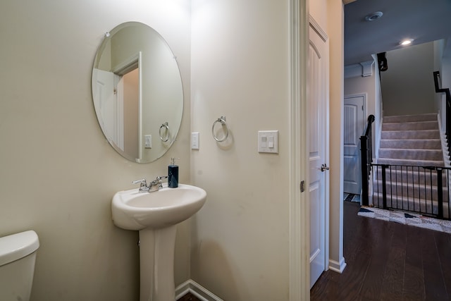 half bath featuring toilet, wood finished floors, baseboards, and a sink