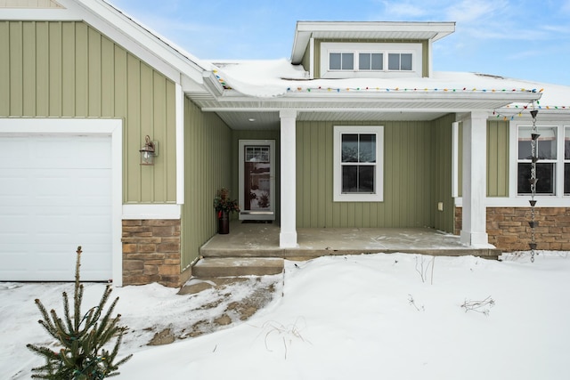 snow covered property entrance with a porch, stone siding, and an attached garage