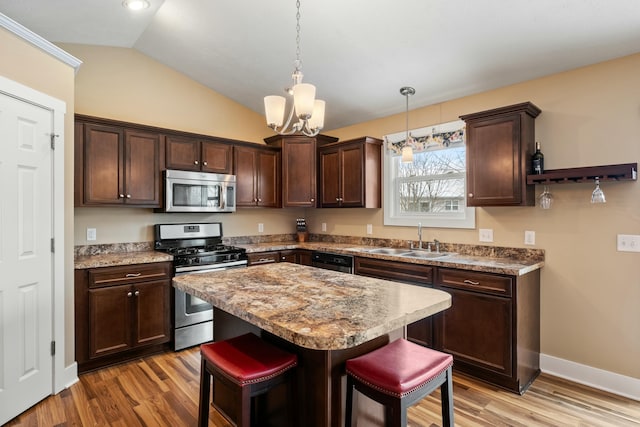 kitchen with stainless steel appliances, a sink, vaulted ceiling, dark brown cabinets, and light wood finished floors