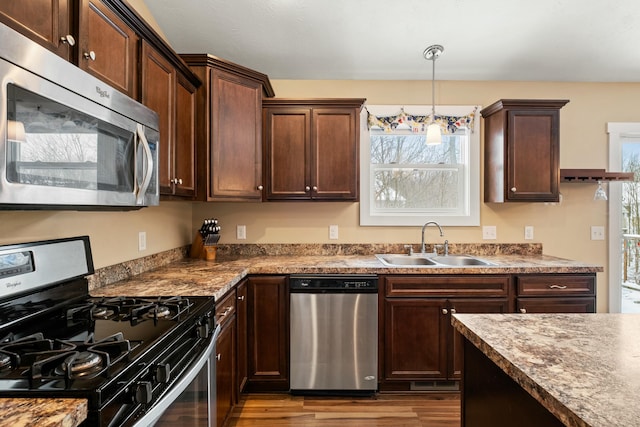 kitchen with pendant lighting, stainless steel appliances, a sink, dark brown cabinets, and wood finished floors