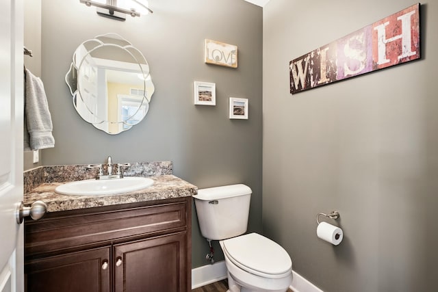 half bath featuring vanity, toilet, and baseboards