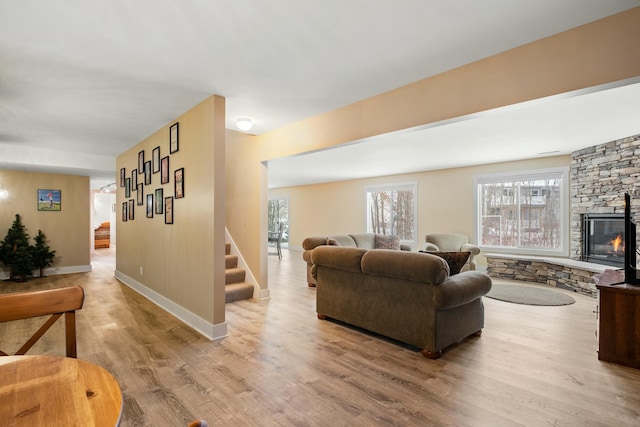 living area featuring light wood-type flooring, stairs, baseboards, and a fireplace