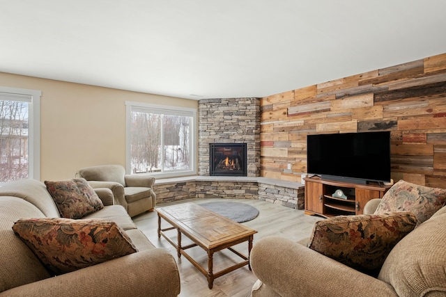 living area featuring a stone fireplace, wood walls, wood finished floors, and a healthy amount of sunlight