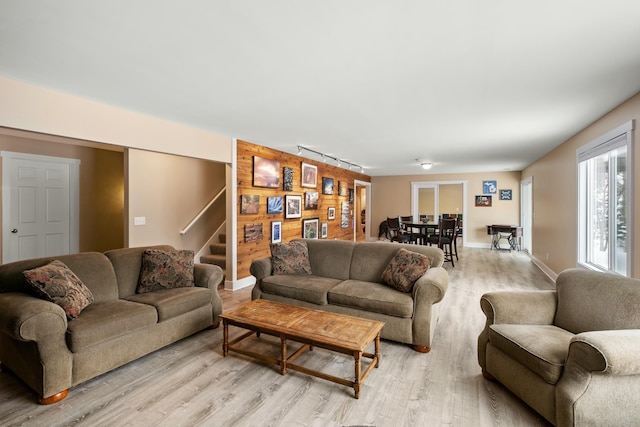 living room with stairs, an accent wall, light wood finished floors, and wood walls