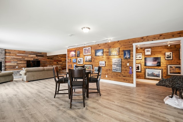 dining area with light wood-type flooring, wood walls, and a fireplace