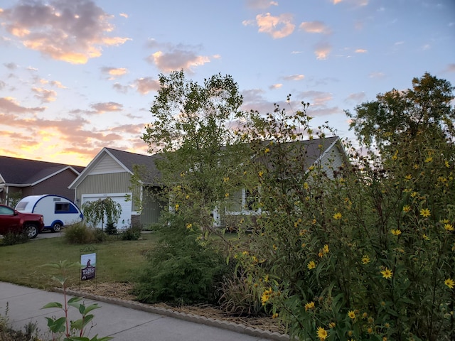 view of property hidden behind natural elements featuring a garage and a yard