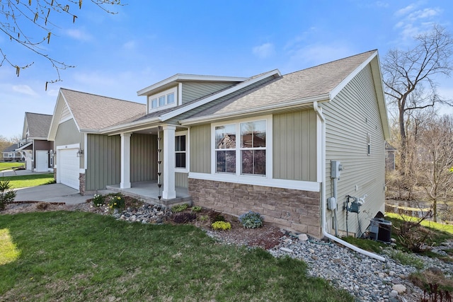 view of front of property with a shingled roof, an attached garage, stone siding, a front yard, and concrete driveway