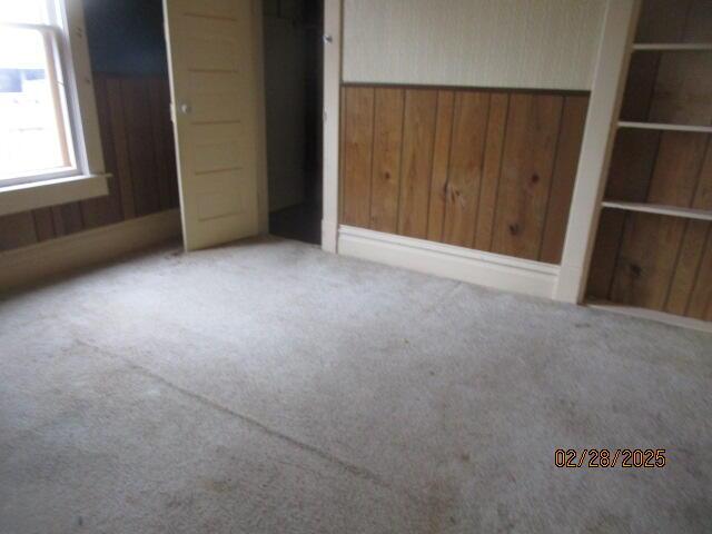 unfurnished bedroom featuring a closet, wood walls, wainscoting, and carpet flooring