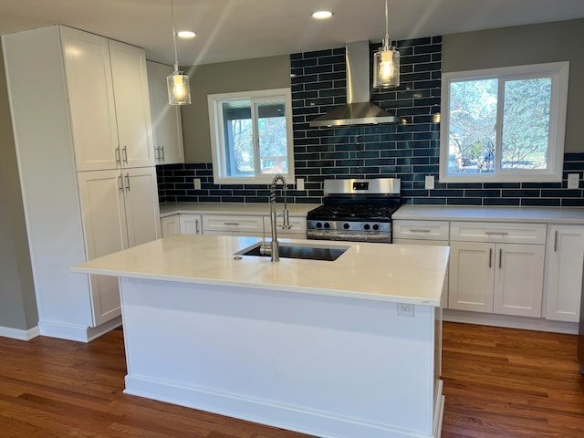 kitchen with white cabinetry, a sink, wood finished floors, stainless steel gas range oven, and wall chimney exhaust hood