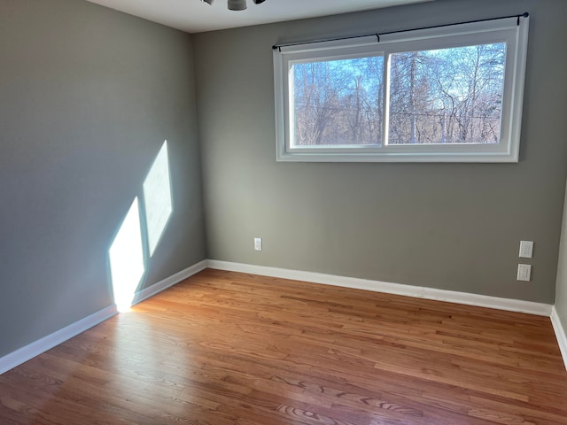 empty room featuring plenty of natural light, wood finished floors, a ceiling fan, and baseboards