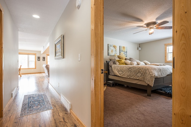 hall featuring a wealth of natural light, visible vents, a textured ceiling, and hardwood / wood-style floors