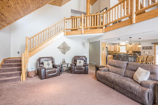 carpeted living room featuring visible vents, baseboards, stairs, wooden ceiling, and a towering ceiling