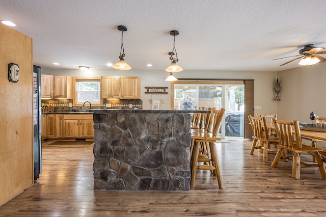 kitchen featuring a kitchen breakfast bar, a ceiling fan, wood-type flooring, and light brown cabinetry