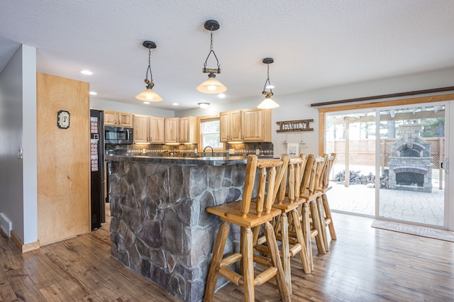 kitchen featuring a kitchen bar, stainless steel microwave, wood finished floors, and light brown cabinetry