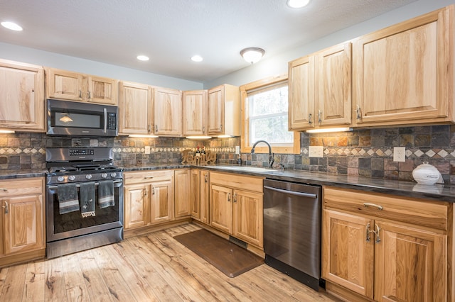 kitchen with light wood finished floors, a sink, light brown cabinetry, stainless steel appliances, and dark countertops