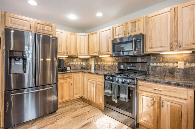 kitchen with light brown cabinets, light wood finished floors, appliances with stainless steel finishes, and tasteful backsplash