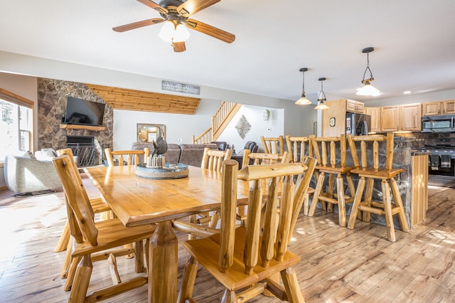 dining space with ceiling fan, a fireplace, stairs, and light wood-style floors