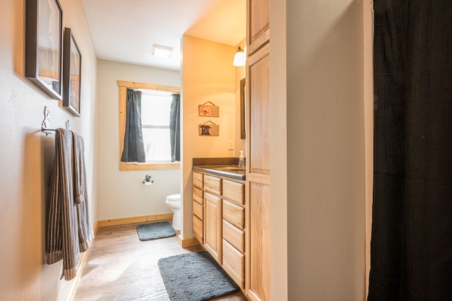 full bath featuring toilet, vanity, baseboards, and wood finished floors