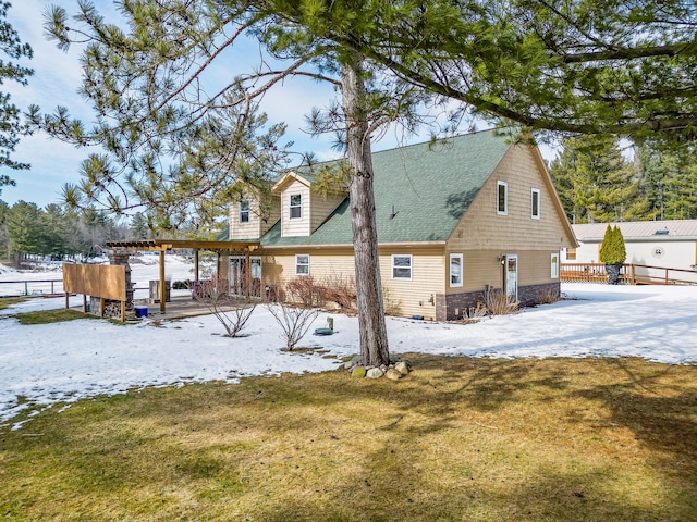 snow covered house featuring a shingled roof, fence, a yard, and a pergola