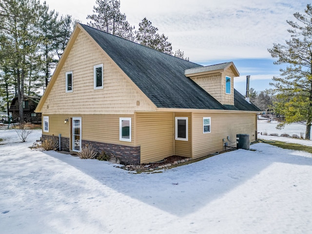 view of snow covered exterior with central air condition unit and roof with shingles