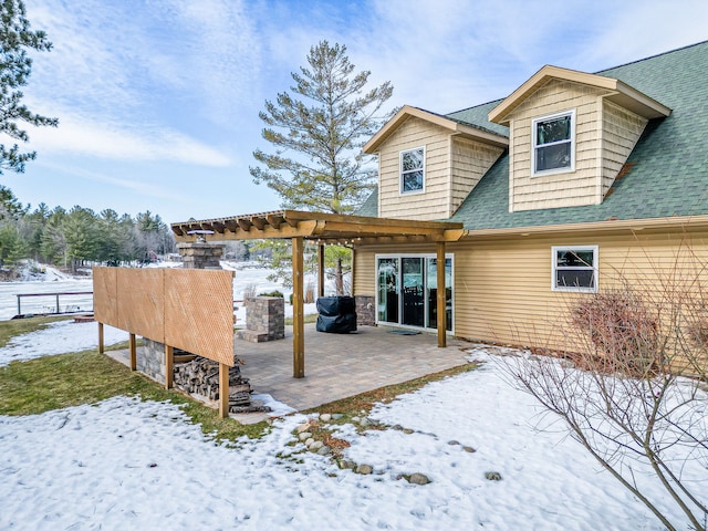 snow covered rear of property featuring a patio and roof with shingles