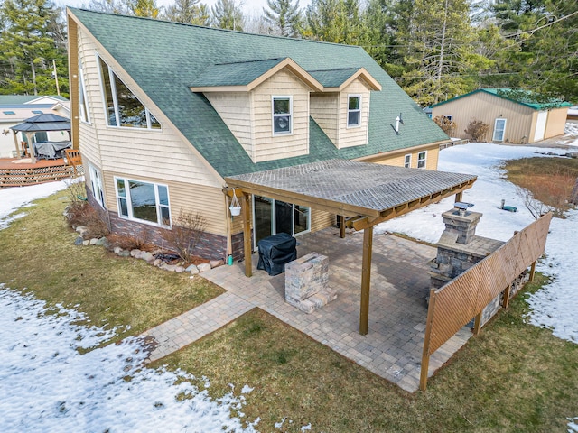 snow covered property with a lawn, a shingled roof, and a patio