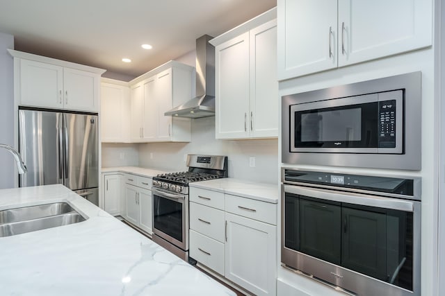 kitchen featuring appliances with stainless steel finishes, white cabinetry, a sink, light stone countertops, and wall chimney exhaust hood