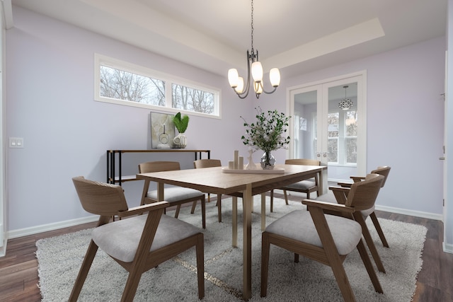 dining space featuring a chandelier, dark wood-style flooring, a raised ceiling, and baseboards