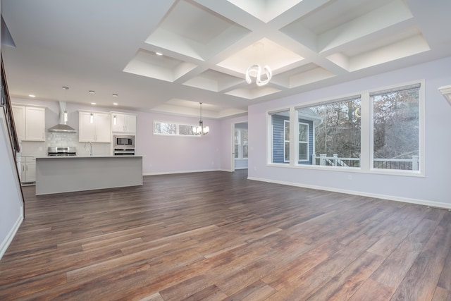 unfurnished living room featuring dark wood-type flooring, a sink, a chandelier, coffered ceiling, and baseboards