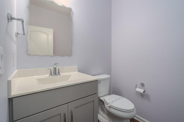 half bathroom featuring toilet, baseboards, and vanity