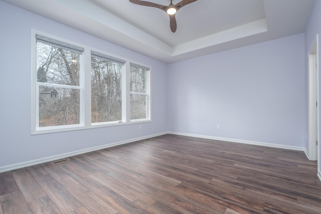 empty room with dark wood-style floors, a tray ceiling, visible vents, and baseboards