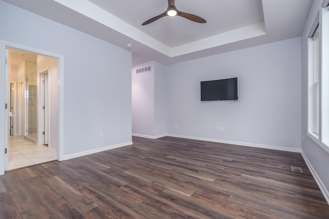 empty room featuring dark wood-type flooring, a tray ceiling, visible vents, and baseboards